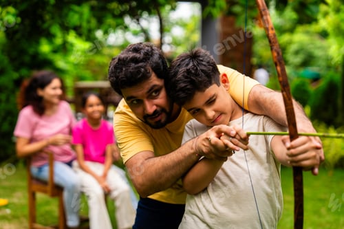 Preview: Homemade bow and arrow fun between Indian father and son in garden during outdoor family time