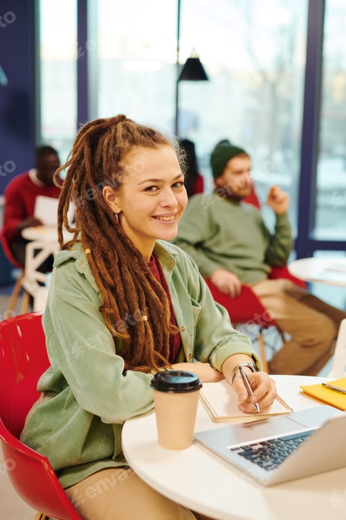 Preview: Happy young contemporary businesswoman with pencil making notes in notebook