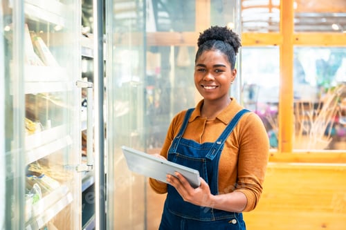 Preview: Smiling saleswoman using digital tablet checking stock in refrigerated section of supermarket
