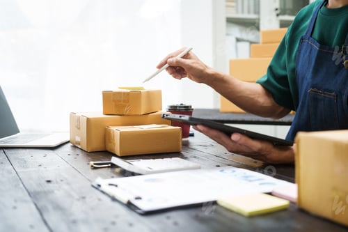 Preview: A man is working at his desk, preparing parcel boxes for shipment. He checks packs items carefully