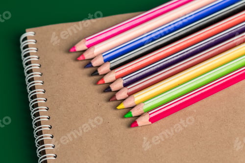 Preview: Colored pencils lay beside a blank notebook on a green background in a simple workspace setup