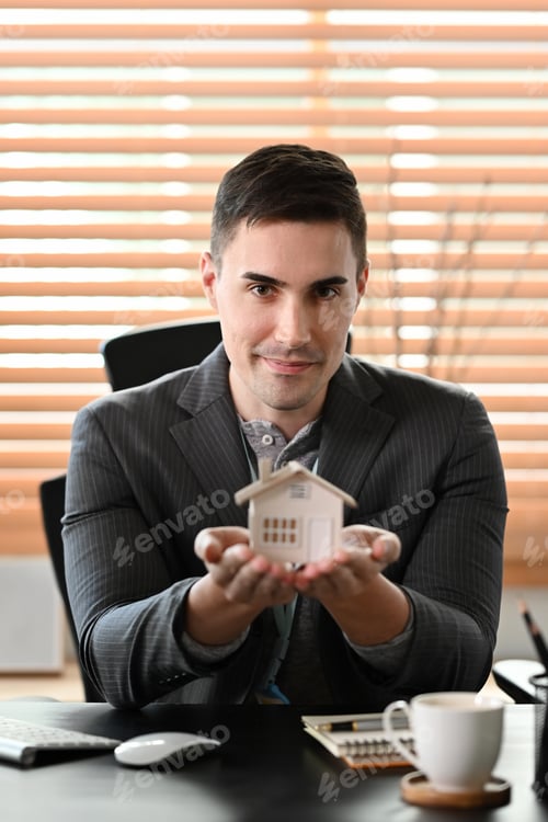 Preview: Portrait of real estate agent holding small house model and looking at camera.