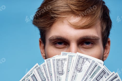 Preview: a man with a wad of money covers his face close-up blue background