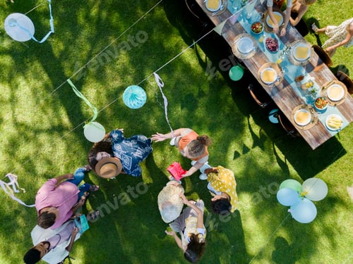 Preview: Top view of a garden party with decorations and set table. The birthday girl greeting guests and