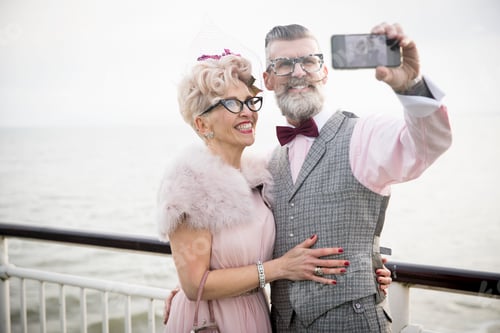 Preview: 1950's vintage style couple taking smartphone selfie on pier