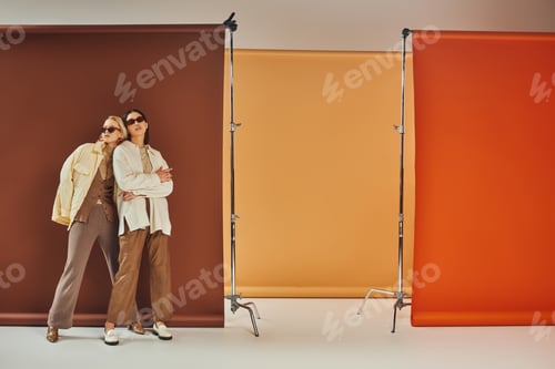 Preview: autumnal season, multiethnic models in sunglasses and fall outerwear posing on colorful backdrop