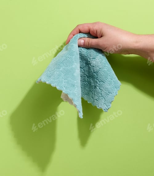 Preview: Female hand holding a bluew rag on a green background