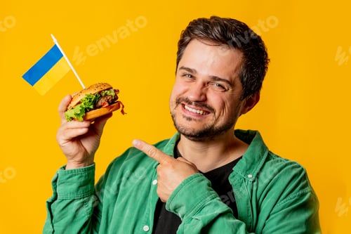 Preview: Happy guy with burger and ukrainian flag on yellow background