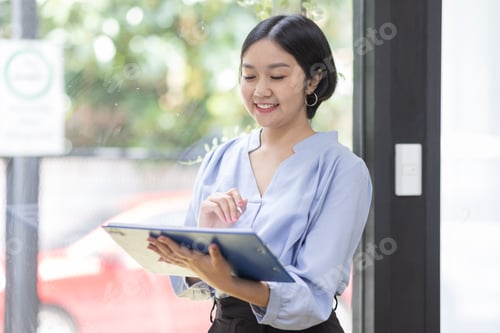 Preview: Boring young business Asian woman holding document file and looking at camera stand on a workplace o