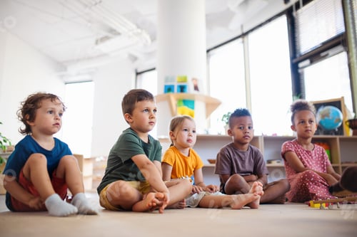 Preview: Group of small nursery school children sitting on floor indoors in classroom