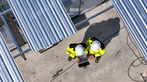 Preview: Two Workers Collaborate on a Laptop Under Solar Panels on a Rooftop