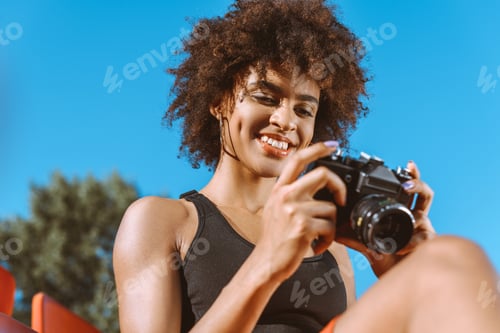 Preview: Young african-american woman looking at the screen of digital photo camera