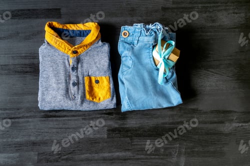 Preview: Different child clothes, pants, accessories with gift box on black wooden table with copy space,