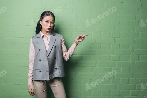 Preview: asian businesswoman pointing at something in front of green wall