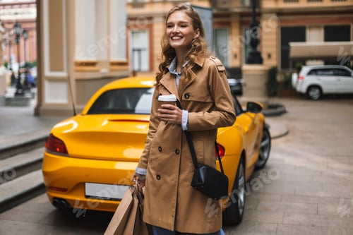 Preview: Pretty smiling girl in trench coat with little black cross bag h