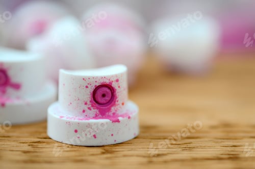Preview: The soiled pink nozzles from the paint sprayer lies on a wooden plank on a background of a many