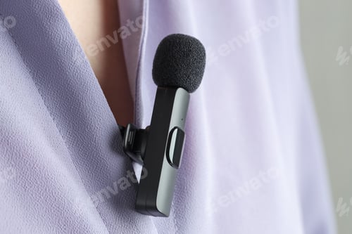 Preview: Woman with lavalier microphone on her shirt against light grey background, closeup