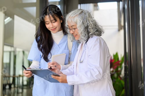 Preview: Old asian woman senior holding chart showing to a young doctor while standing or walking in clinic.
