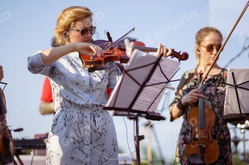 Preview: Charming woman playing violin in orchestra at outdoor concert