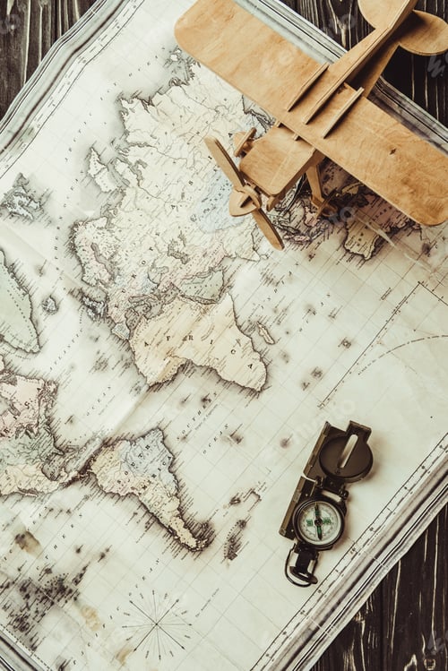 Preview: top view of map, wooden toy plane and compass on dark wooden surface