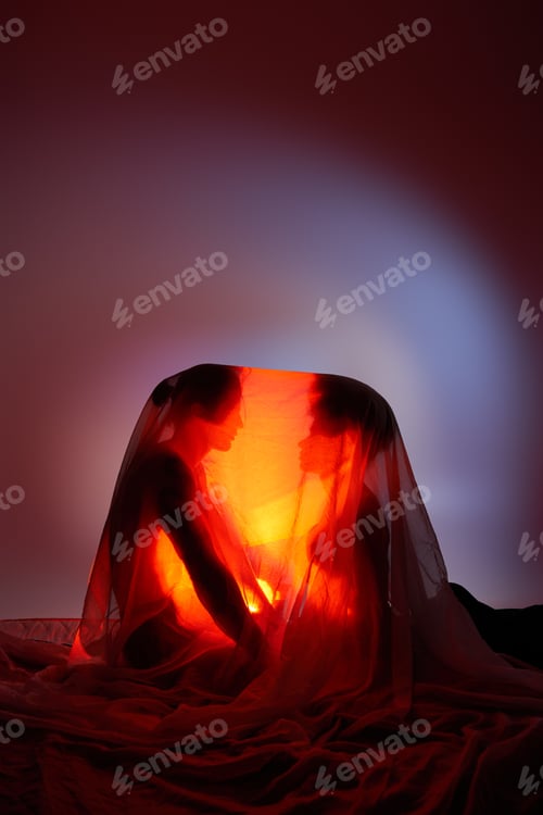 Preview: sexy diverse couple covered with bedsheet surrounded by light on gray background, togetherness