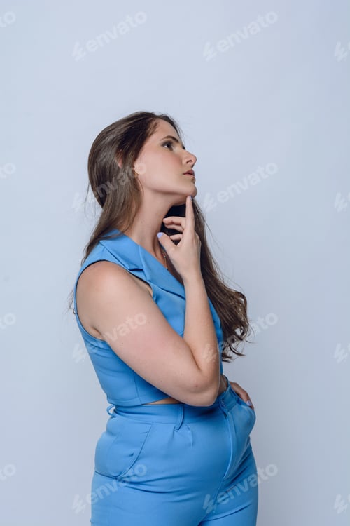 Preview: portrait of young latin woman in blue executive clothing posing with hand on chin, studio shot