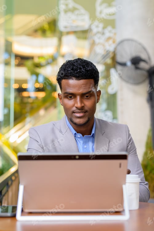 Preview: African businessman at coffee shop using laptop computer vertical shot