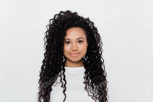 Preview: Curly african american woman in white t-shirt looking at camera isolated on grey
