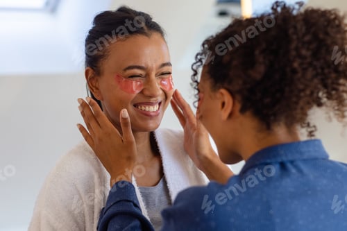 Preview: Happy biracial lesbian couple in bathrobes wearing eye masks in bathroom