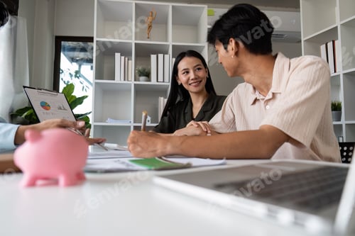 Preview: Young Couple Planning Finances Together with Piggy Bank and Laptop in Modern Home Office Setting