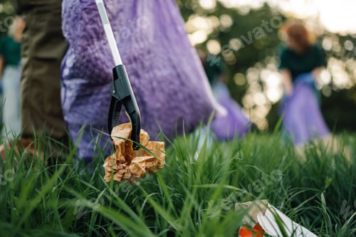 Preview: Person picking up trash with grabber tool in the grass