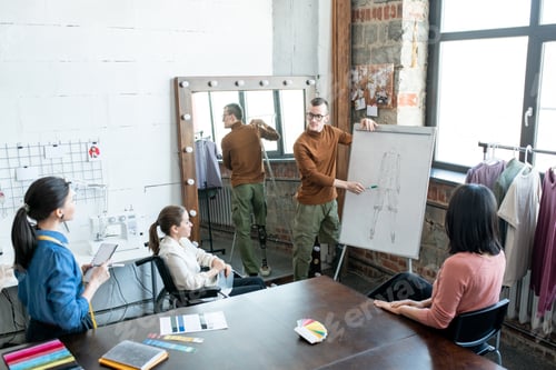 Preview: Young disable male designer pointing at sketch on whiteboard while making presentation to colleagues