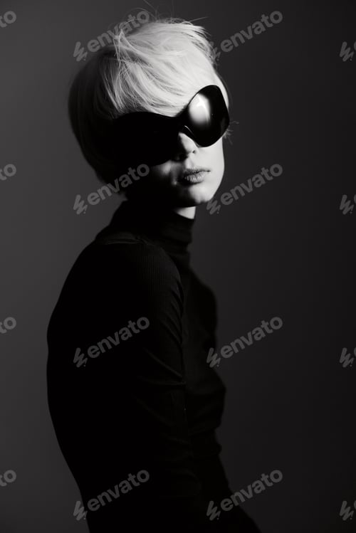 Preview: Stylish young woman with short blonde hair and large black sunglasses posing elegantly against a