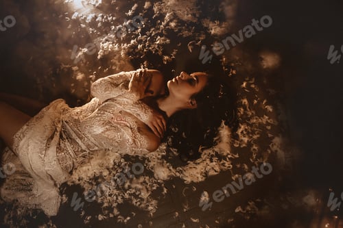 Preview: Young beautiful woman in a peignoir lies in feathers on the floor