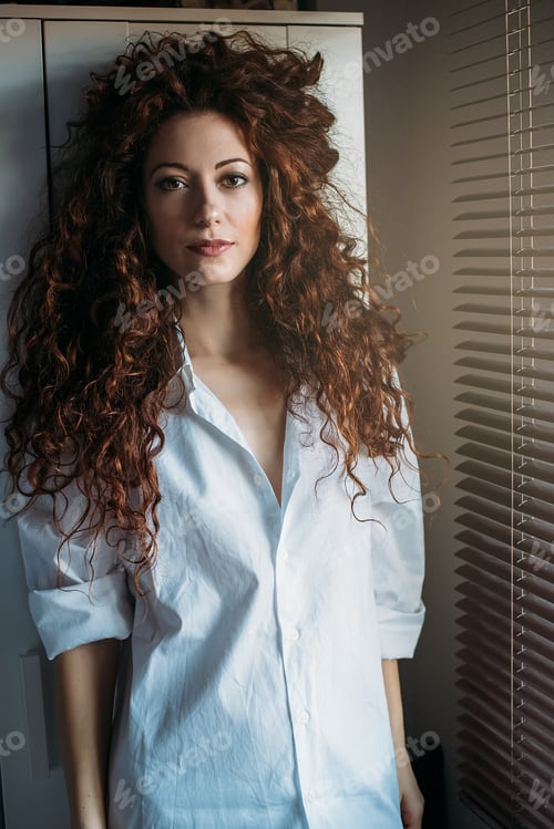 Preview: Beautiful thoughtful woman standing by a windows blind