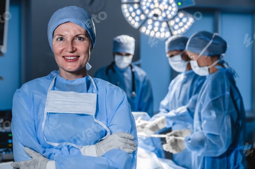 Preview: Portrait of caucasian female doctor with blur background of medical team doing surgical operation