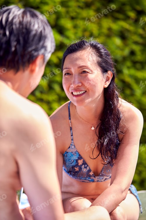 Preview: Mature Couple Talking On Loungers Relaxing By Swimming Pool On Summer Vacation