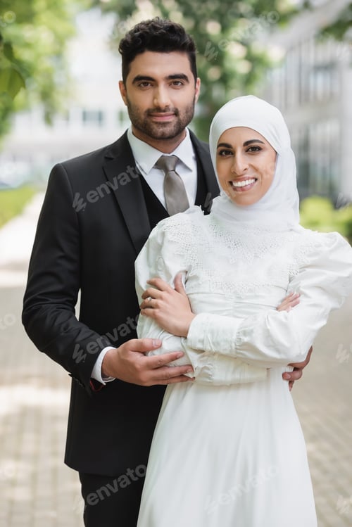 Preview: happy groom hugging muslim bride in hijab with wedding ring