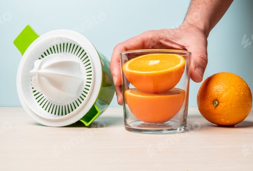 Preview: Closeup shot of freshly cut oranges in a glass next to a juicer