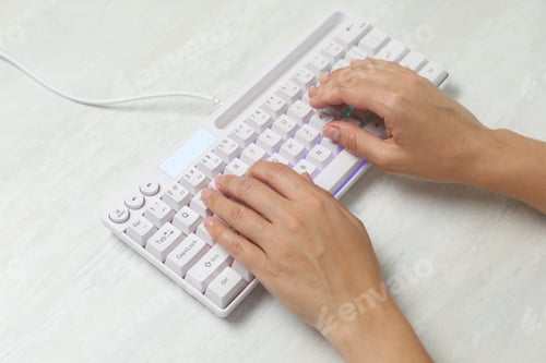 Preview: Woman typing on modern keyboard with RGB lighting at white wooden table, closeup