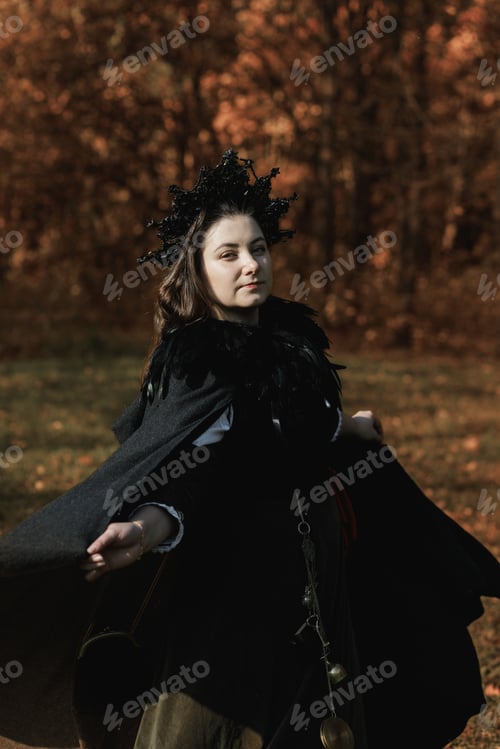 Preview: Young woman in medieval dress and cloak standing by tree in forest. Middle Ages