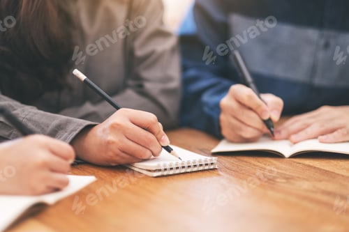 Preview: Closeup image of many people writing on blank notebook together on wooden table