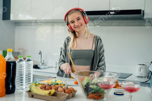 Preview: Happy teenage girl listen to music and cooking in kitchen.