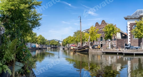 Preview: Tranquil canal with historic buildings and trees in Schiedam, Netherlands, with a boat moored