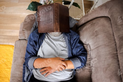 Vista previa: Senior Man Sleeping While Covering Face With Book on Sofa