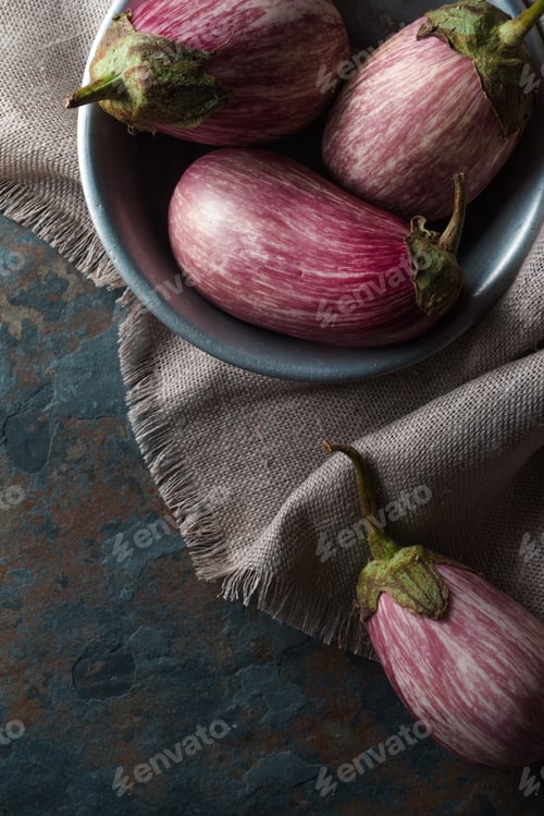Preview: Colored eggplant in a tin bowl on a linen napkin on a blue stone