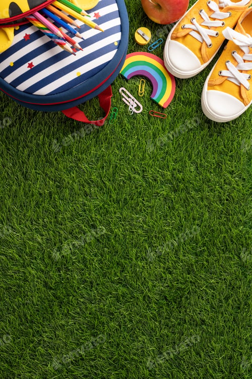 Preview: Back to school concept showing a backpack, yellow shoes, and school supplies on vertical green grass