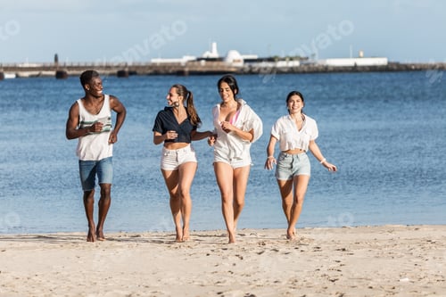 Preview: Happy multiethnic friends running along beach in summer