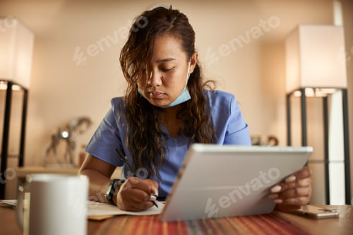 Preview: filipina nurse working from home doing paperwork and using tablet