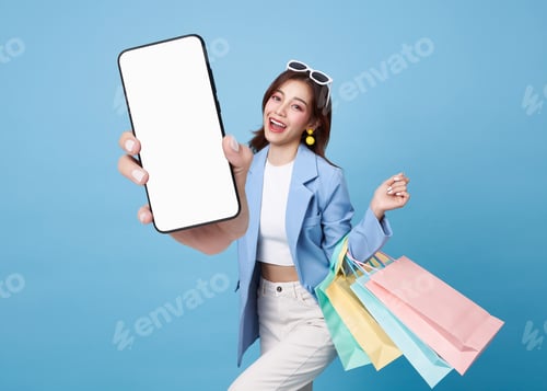 Preview: Asian woman holding shopping bags and showing blank smartphone screen for online shopping